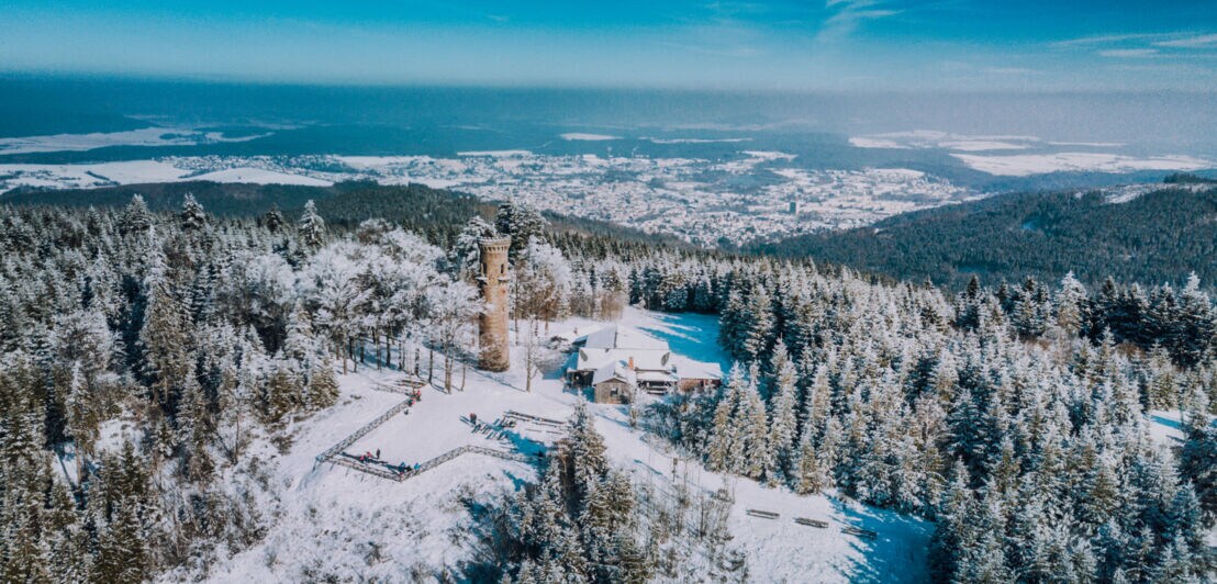 Luftaufnahme eines verschneiten Berges in einem Mittelgebirge mit einem Turm auf dem Gipfel