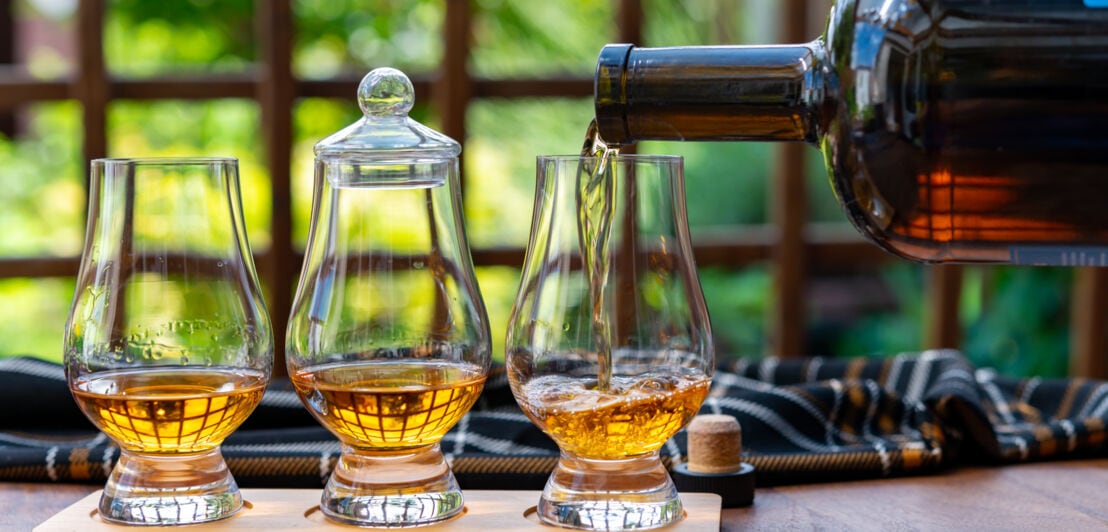 Drei Whiskygläser, die aus einer Flasche befüllt werden