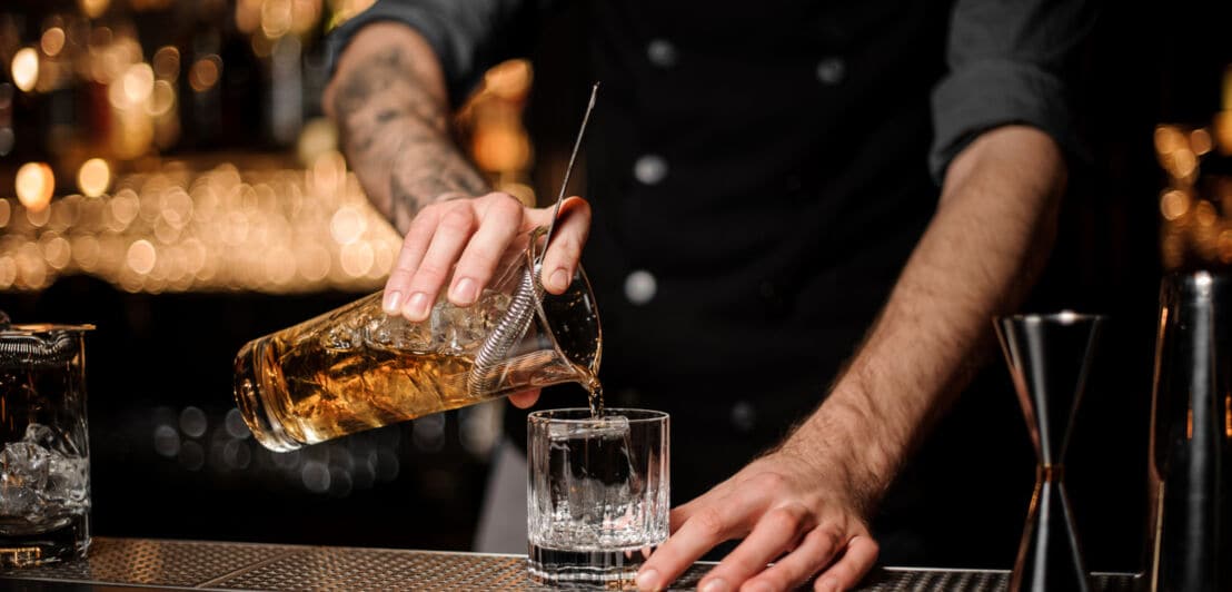 Ein Bartender füllt einen Whiskycocktail aus einem Shaker in ein Glas
