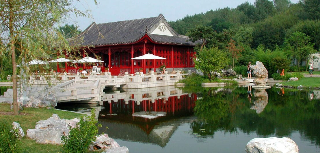 Ein See umgeben von Bäumen mit einem Gebäude im chinesischen Stil am Seeufer