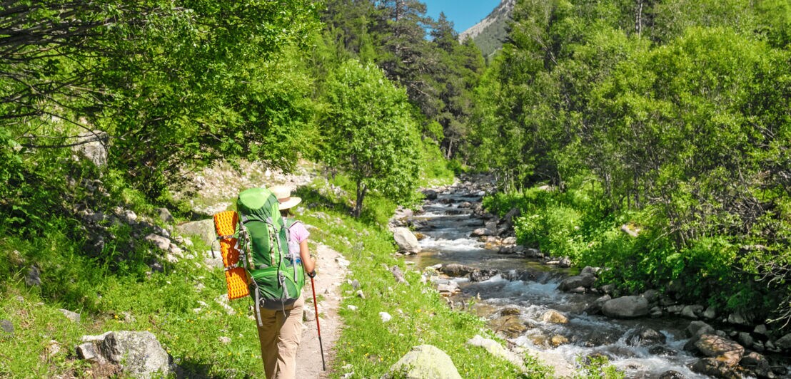 Eine Wanderin läuft neben einem kleinen Fluss in den Pyrenäen
