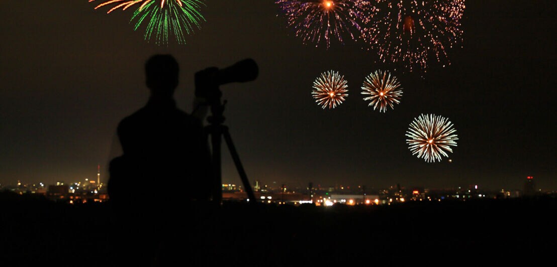 Die Silhouette eines Mannes vor einer Kamera vor einem Feuerwerk über einer Stadt