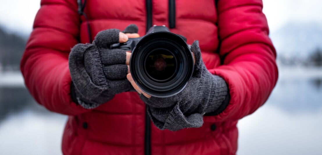 Eine Person in roter Jacke und mit Handschuhen hält eine Kamera