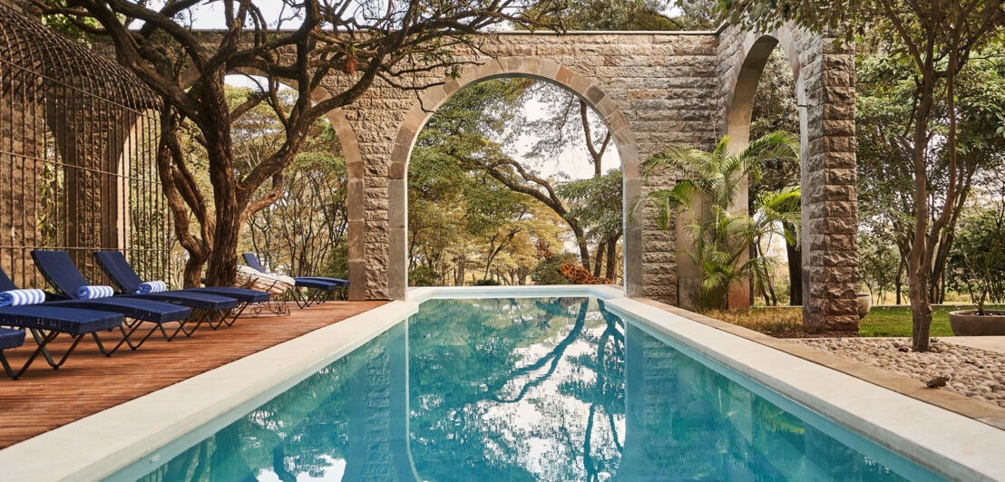 Ein langer Outdoor-Pool mit Rundbögen und einer Giraffe im Hintergrund