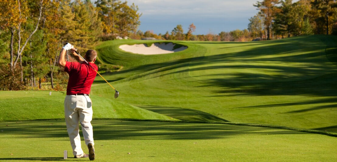 Ein Mann in rotem T-Shirt hat einen Ball auf einem Golfplatz geschlagen