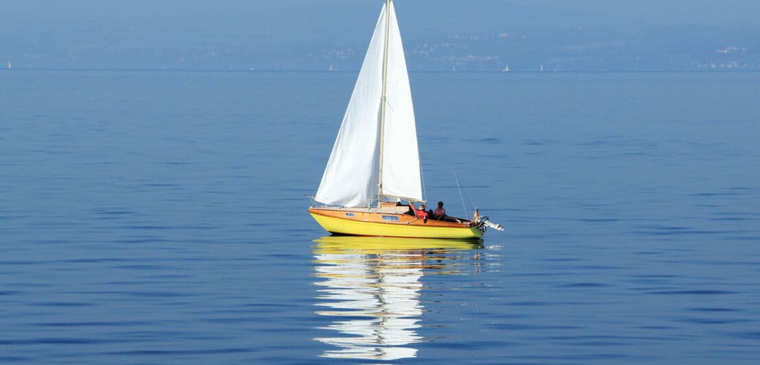 Eine kleine Jacht mit mehreren Personen an Bord vor einer Küste