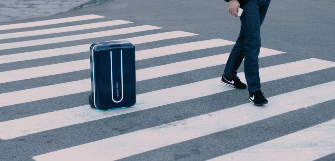 Ein Mann läuft über einen Zebrastreifen, neben ihm rollt sein Koffer