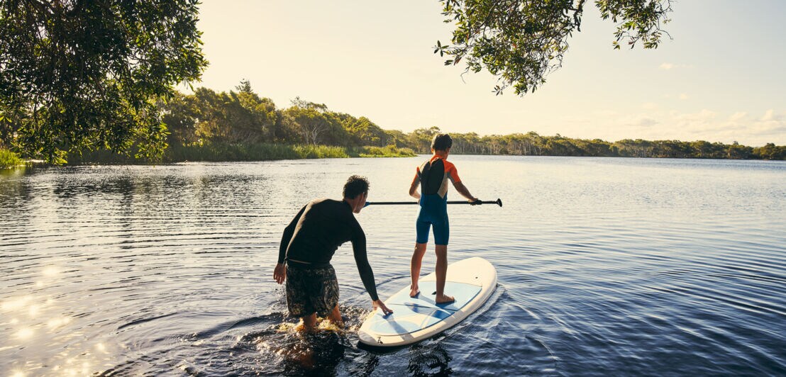 Ein Junge steht auf einem SUP-Board auf einem See