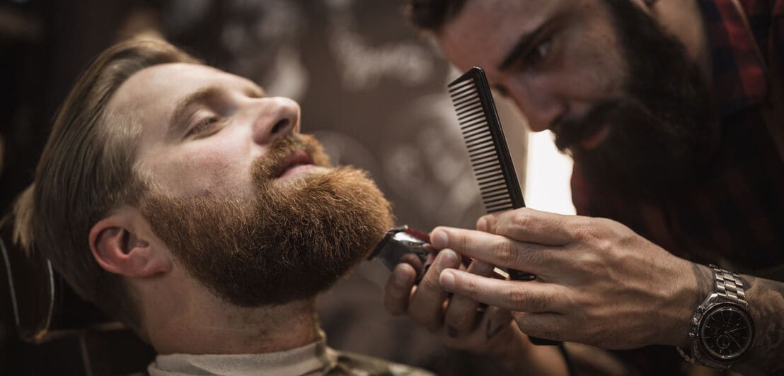Ein Mann bekommt seinen Vollbart von einem Barbier getrimmt