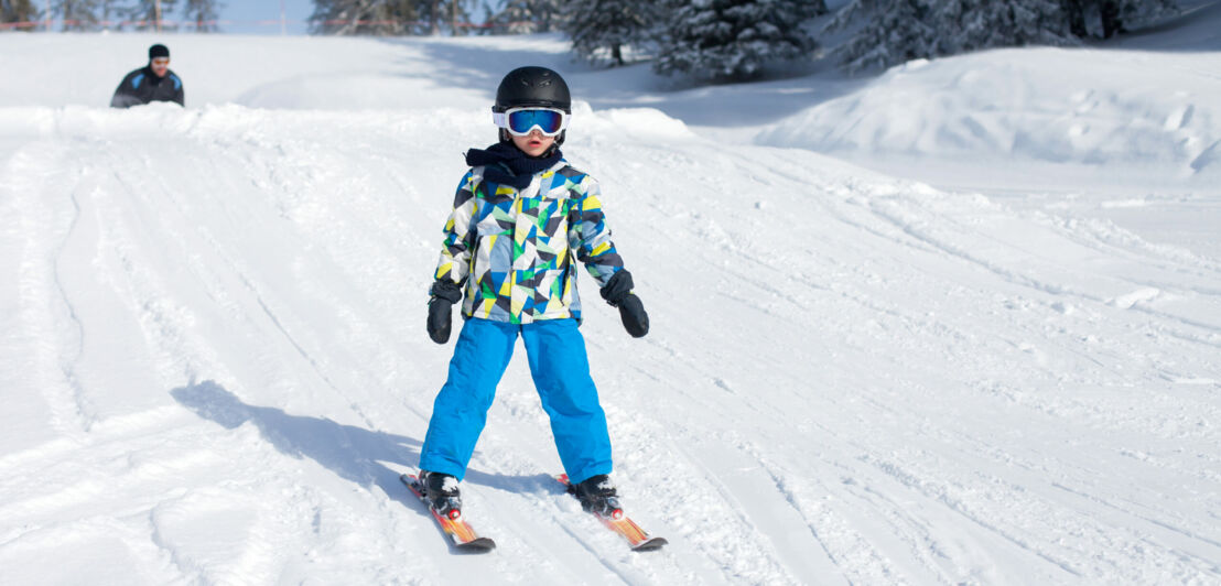 Ein Kind steht auf Skiern in einer Schneelandschaft.