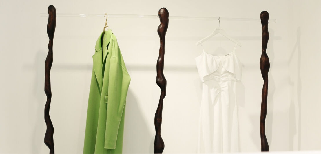 Ein limonengrüner Mantel hängt neben einem weißen Trägerkleid auf einer besonderen Kleiderstange im William-Fan-Store