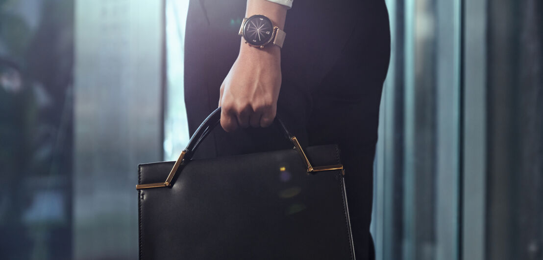 Eine Frau mit eleganter Armbanduhr trägt eine Ledertasche