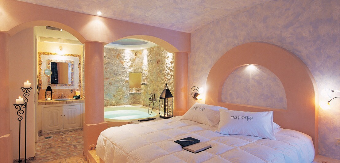 Hotelzimmer in Pastelltönen mit großem Bett und Whirlpool im Hintergrund