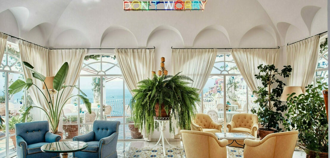 Eine helle Bar mit Panoramafenstern, gemütlichen Sesseln und einer Neonlicht-Installation mit dem Schriftzug “Don’t Worry”