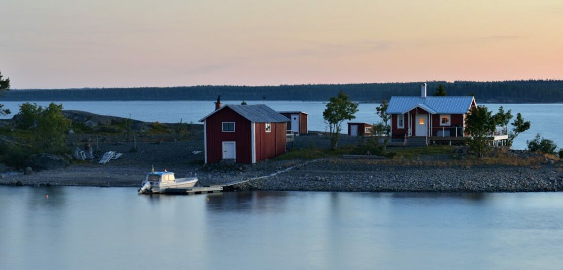 Eine schwedische Insel mit einem roten Holzhaus mit Bootsanleger in der Dämmerung