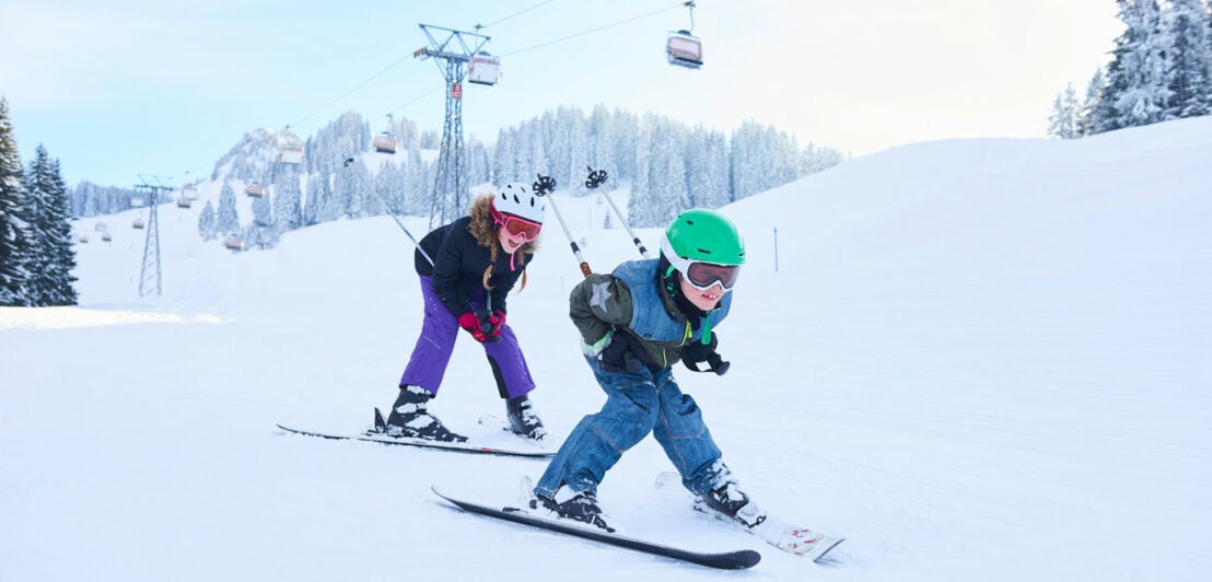 Zwei Kinder fahren Ski auf einer Piste in Gstaad.