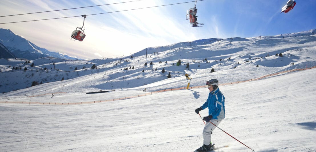 Ein Skifahrer fährt bei Sonnenschein eine Piste hinab.