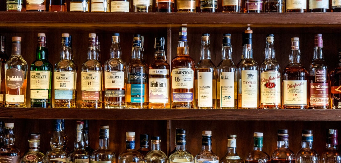 Zahlreiche verschiedene Scotch-Whisky-Flaschen auf drei Regalfächern