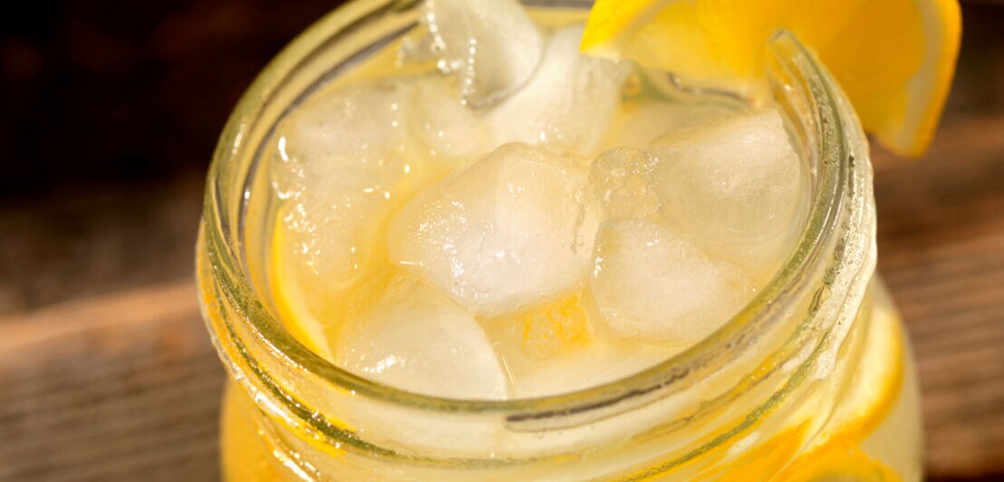 Detailaufnahme einer Limonade im Glas mit Eiswürfeln und Zitronenscheibe