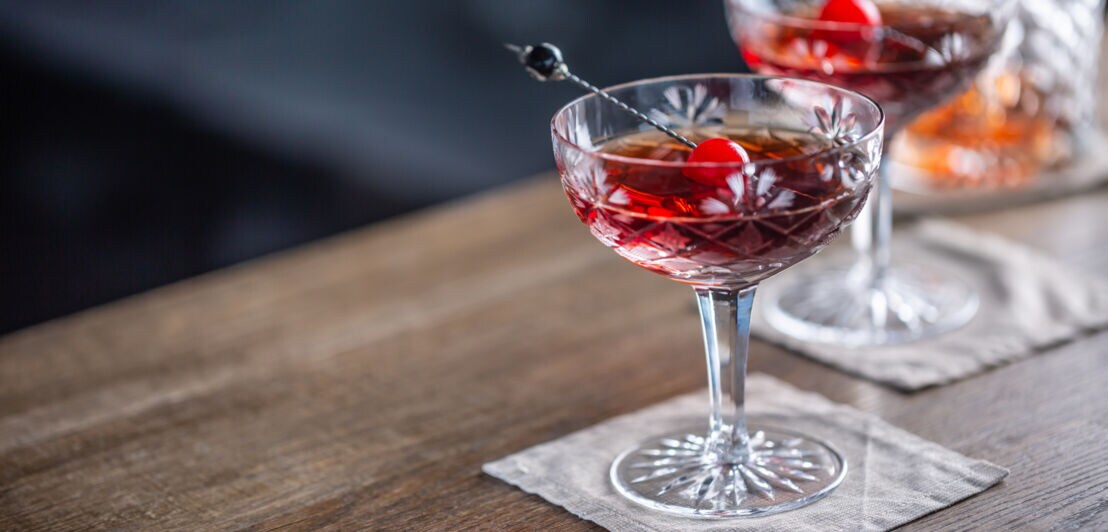 Zwei rote Cocktails in Martinigläsern, garniert mit Kirsche