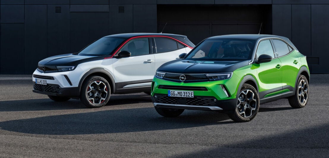 Zwei Opel Mokka mit Zweifarblackierung stehen nebeneinander – der rechte in Grün mit schwarzem Dach samt Motorhaube, der linke in Weiß mit Schwarz.