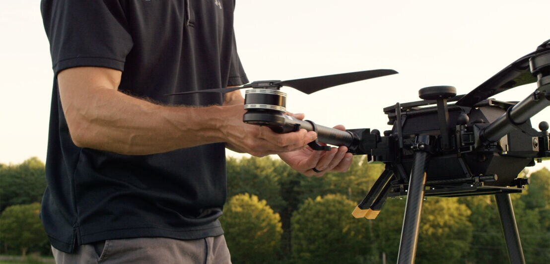 Ein Mann steht neben einer schwarzen Drohne und justiert einen Arm