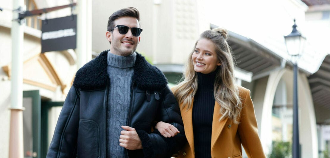 Ein junges, lachendes Paar geht Arm in Arm durch eine Einkaufsstraße