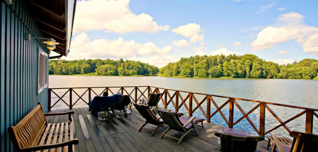 Eine Terrasse mit Liegestühlen an einem Holzhaus am Ufer eines Sees