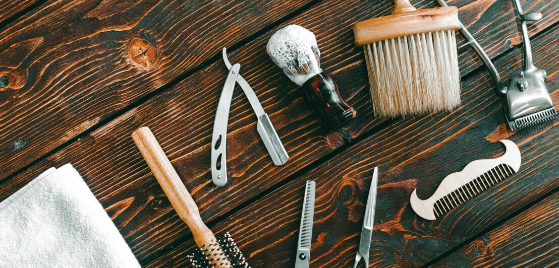 Unterschiedliche Accessoires für Rasur und Bartpflege liegen auf einem Holztisch.