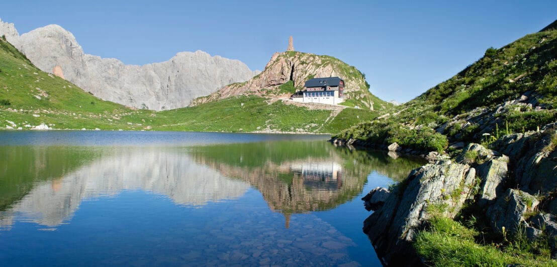 In einem See spiegelt sich eine Hütte und eine Kalkwand