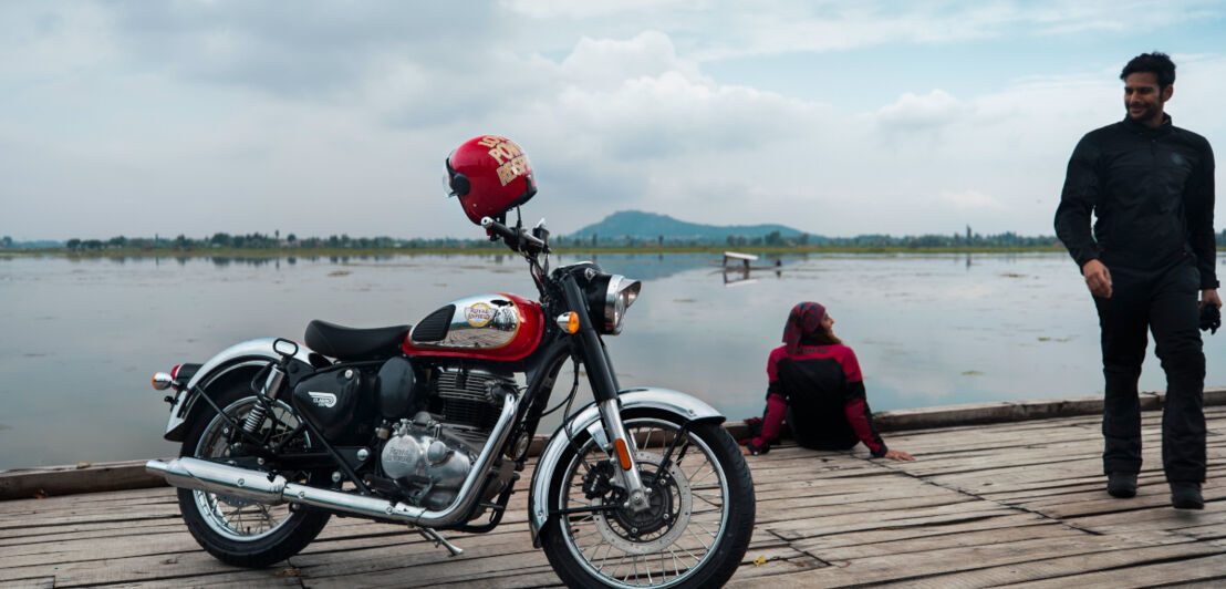 Ein Motorrad, ein Mann und eine Frau auf einem Steg vor einem See