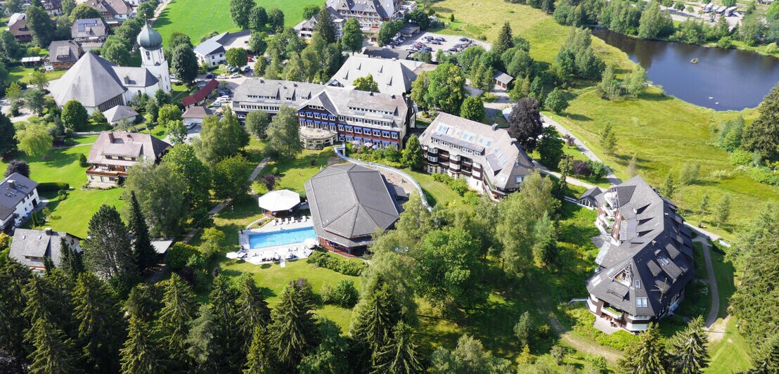 Herrschaftliches Anwesen und Hotelkomplex mit Swimmingpool in begrünter Umgebung mit Wald und See aus der Vogelperspektive
