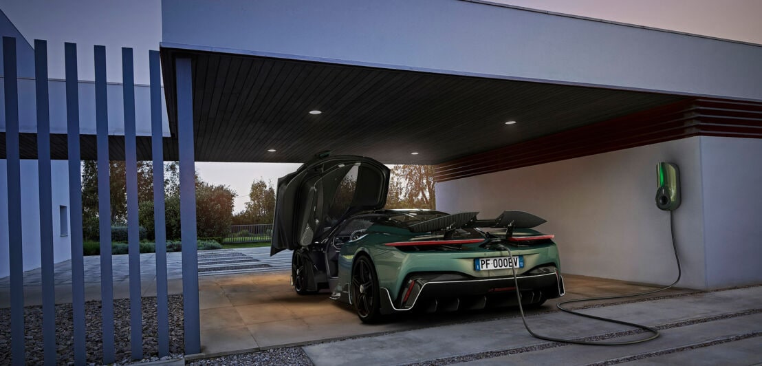 Ein dunkelgrüner Sportwagen, dessen Türen, Heckspoiler und Motorhaube geöffnet ist, lädt an einem überdachten Stellplatz an einer farblich dem Auto entsprechenden Ladestation.
