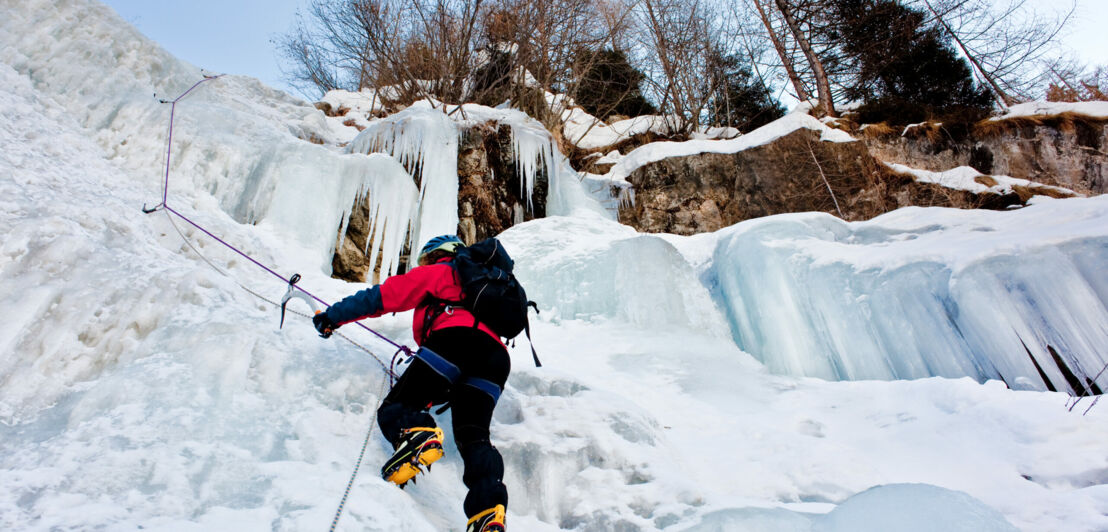 Eine Person klettert einen steilen gefrorenen Wasserfall hinauf.
