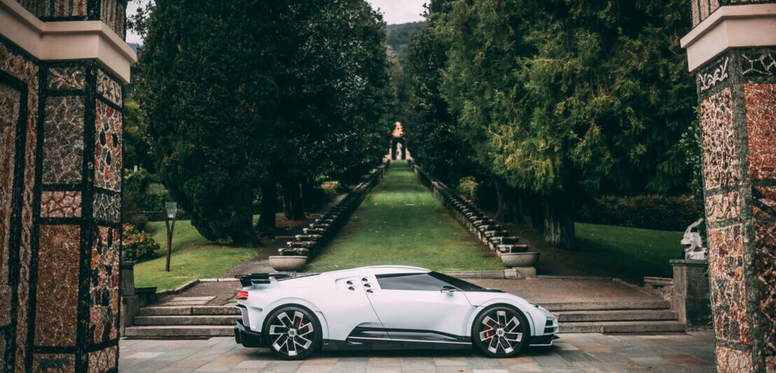 Ein weißer Bugatti steht vor einem parkähnlichen Anwesen