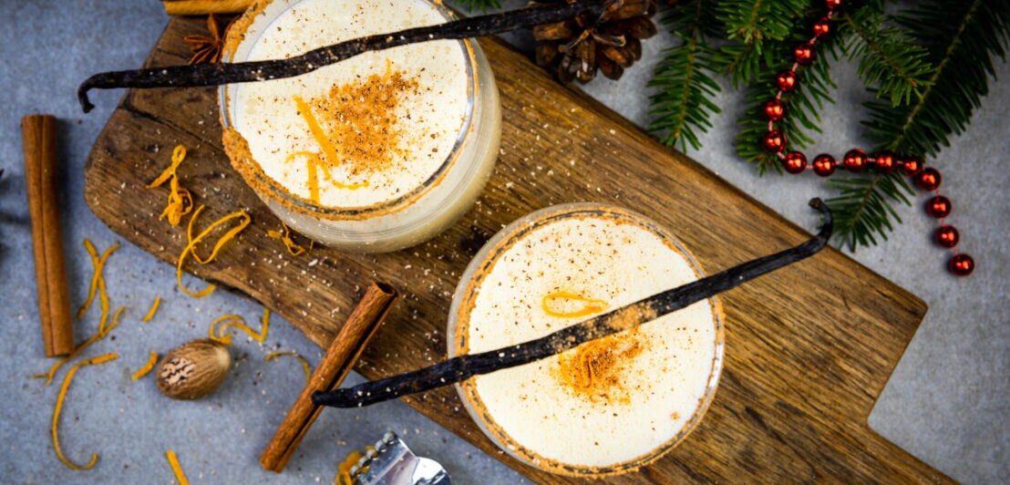Zwei Gläser mit einem weihnachtlichen Heißgetränk mit Milch, Sahne, Zimt, Vanille, Muskat und Sahne, weihnachtlich dekoriert