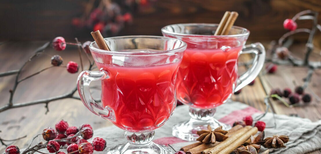 Zwei Gläser mit einem roten Heißgetränk aus Cranberrysaft, dekoriert mit winterlichen Zweigen, Zimtstangen und Sternani