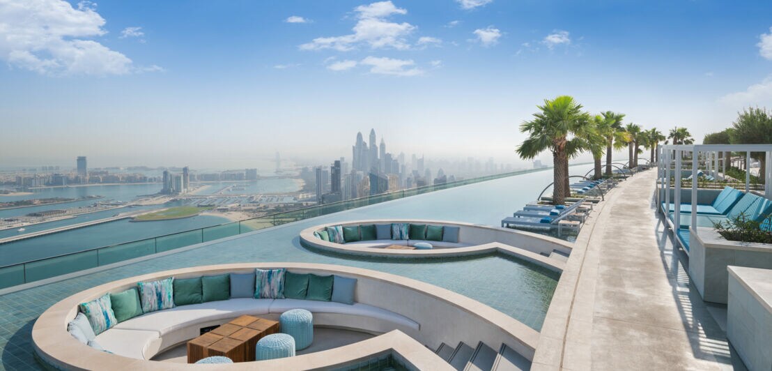 Ein langgestreckter Pool mit eingelassenen runden Sitznischen und Blick auf den Ozean sowie die Skyline Dubais