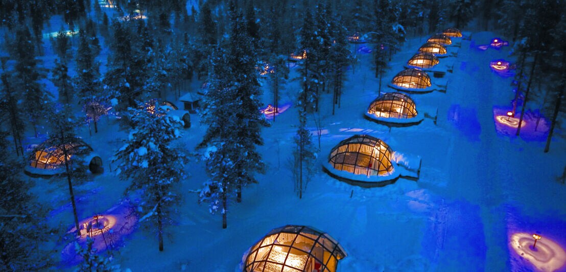 Beleuchtete Glas-Iglus in weitläufiger Schneelandschaft bei Nacht aus der Luft betrachtet
