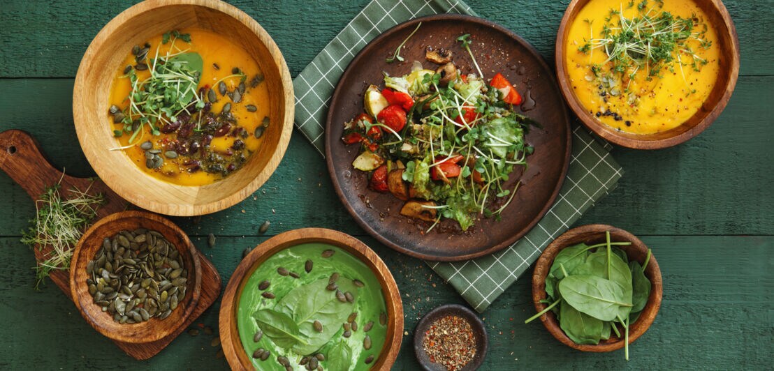 Top-Shot diverser pflanzlicher Gerichte mit Körnern, angerichtet in Holzschalen auf grünem Holzuntergrund