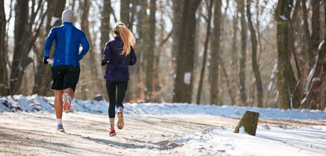 Ein Läufer und eine Läuferin von hinten fotografiert in einer Winterlandschaft