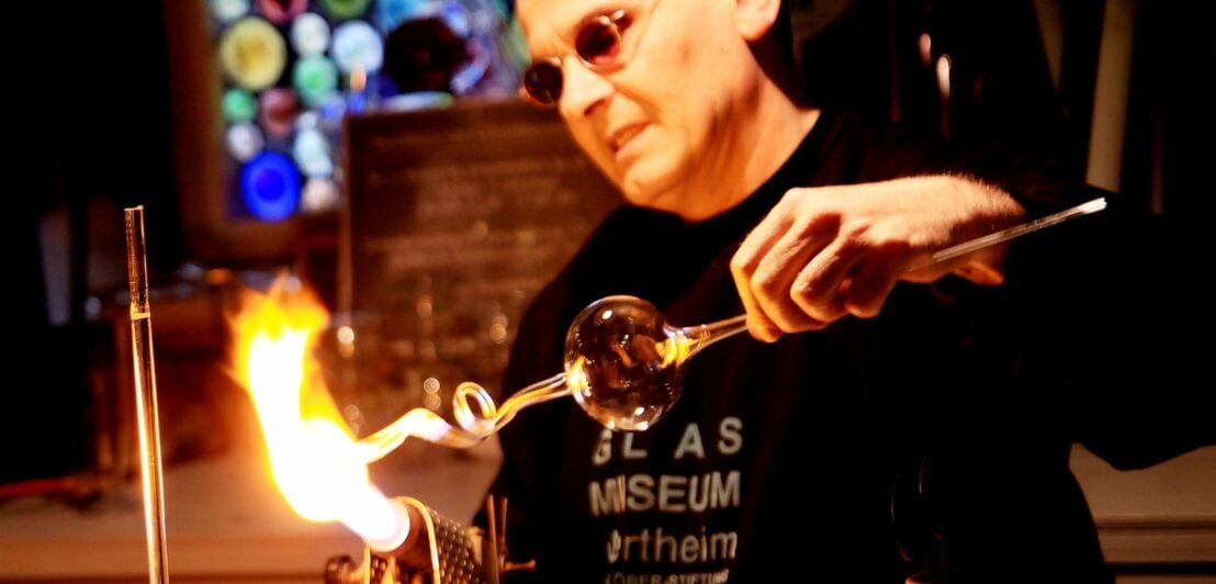 Ein Mann hält ein geblasenes Glasstück in eine Flamme