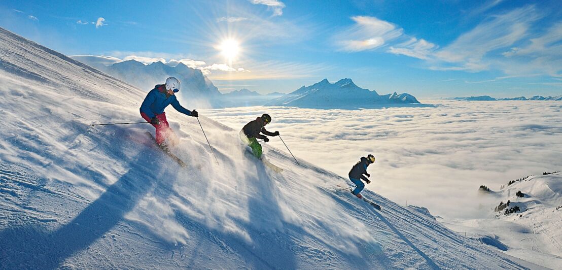 Drei Skifahrer:innen bei der Abfahrt im freien Gelände
