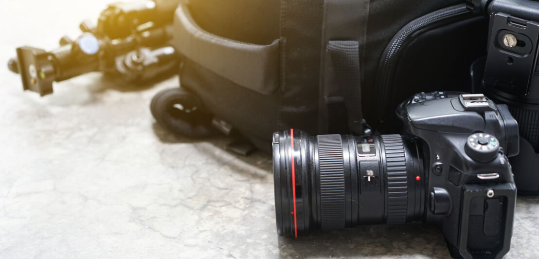 Ein Fotoapparat liegt neben einem Rucksack mit einer Fotoausrüstung.