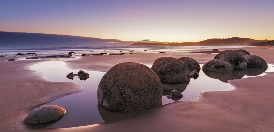 Große Steinkugeln am Strand, im Hintergrund geht die Sonne unter
