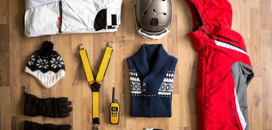 Handschuhe, Mütze, Jacke, Pullover, Helm, Hose, Skibrille und GPS-Gerät liegen auf dem Boden