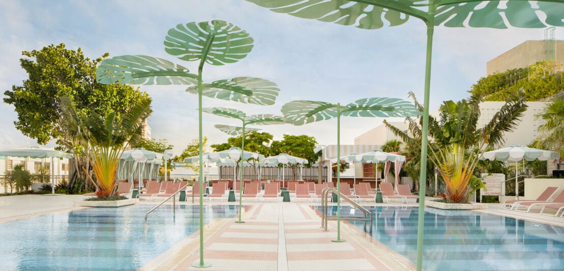 Ein Pool, umgeben von Palmen, blauem Himmel und Liegestühlen in Zartrosa