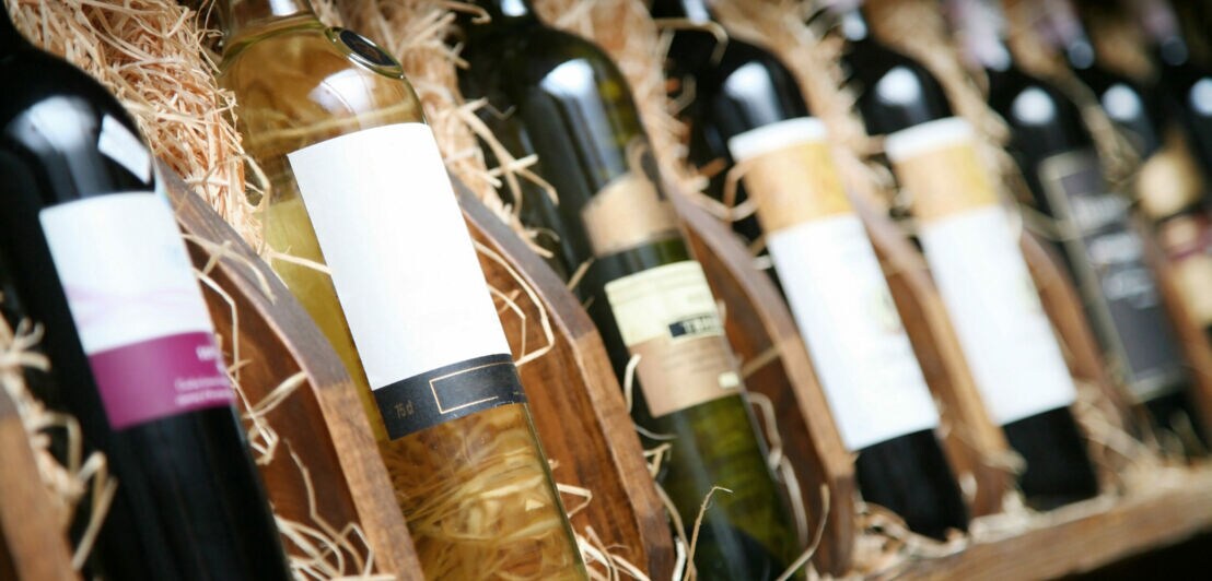 Mehrere Weinflaschen aufgereiht in einer Holzkiste, auf Stroh gebettet.