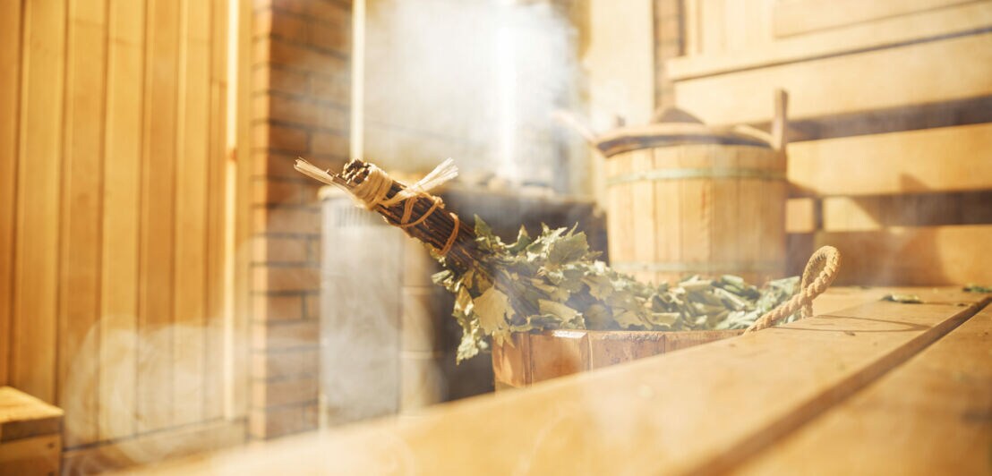 Innenraum einer finnischen Sauna aus Holz, aus einem Holzeimer mit Zweigen steigt Dampf auf