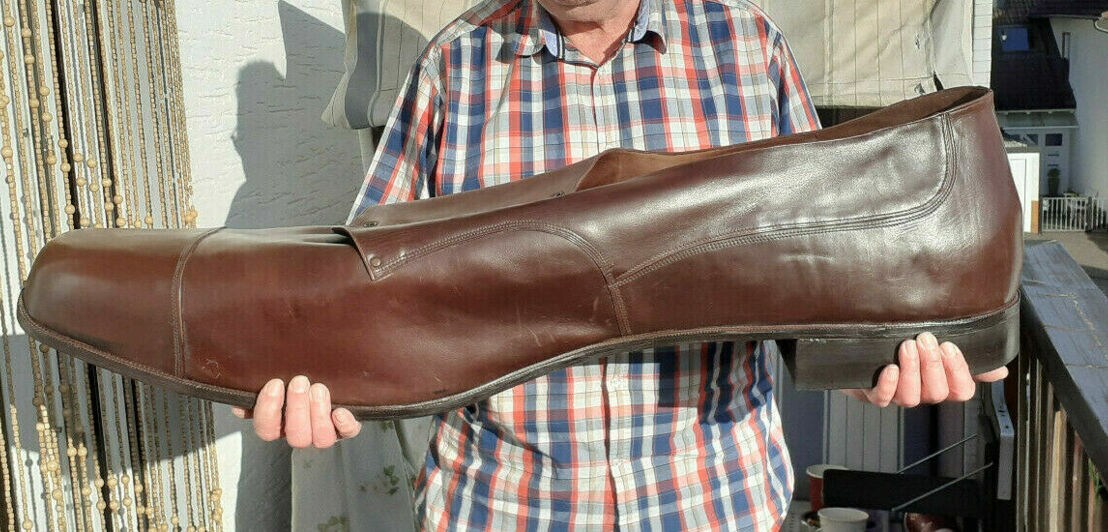 Ein Mann hält einen braunen Lederschuh in Schuhgröße 150